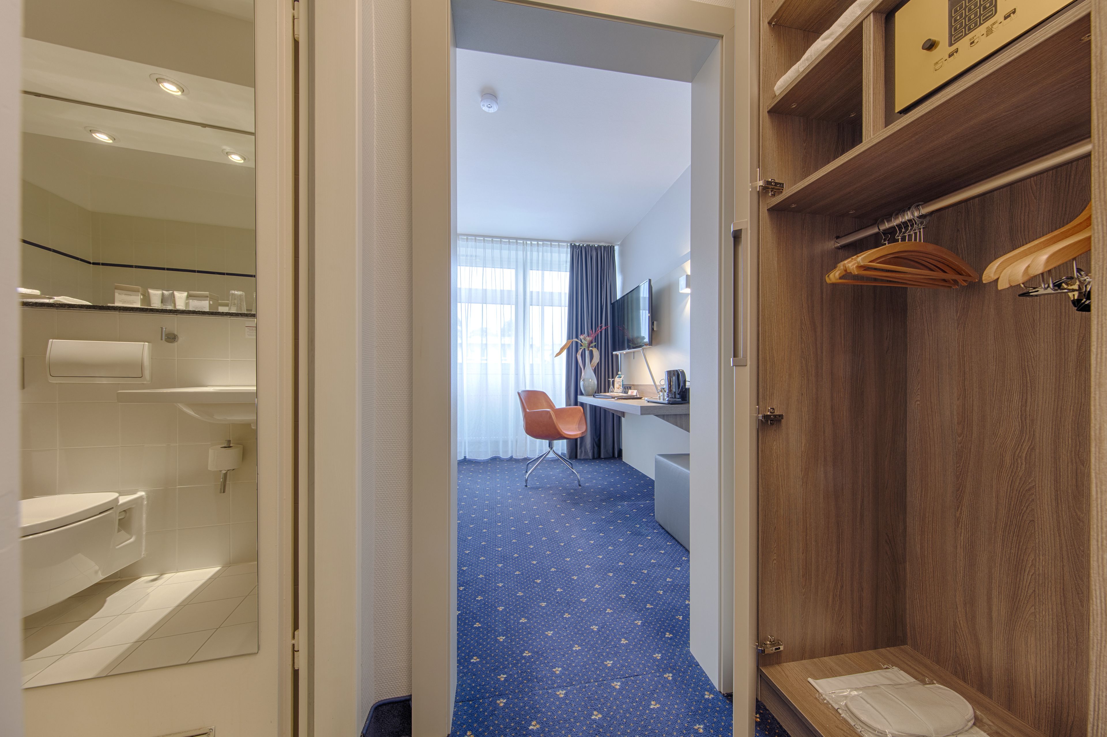 Habitación de hotel con baño, un escritorio y silla, televisor y armario.