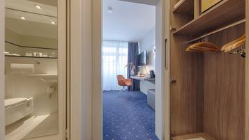 Habitación de hotel con baño, un escritorio y silla, televisor y armario.