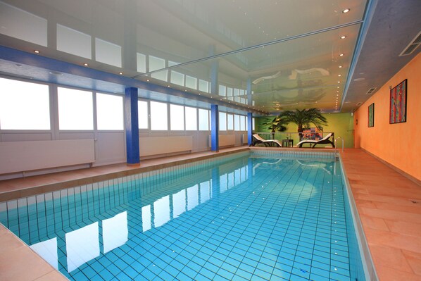Una piscina interior con azulejos azules cristalinos, techo de vidrio y vistas al cielo.