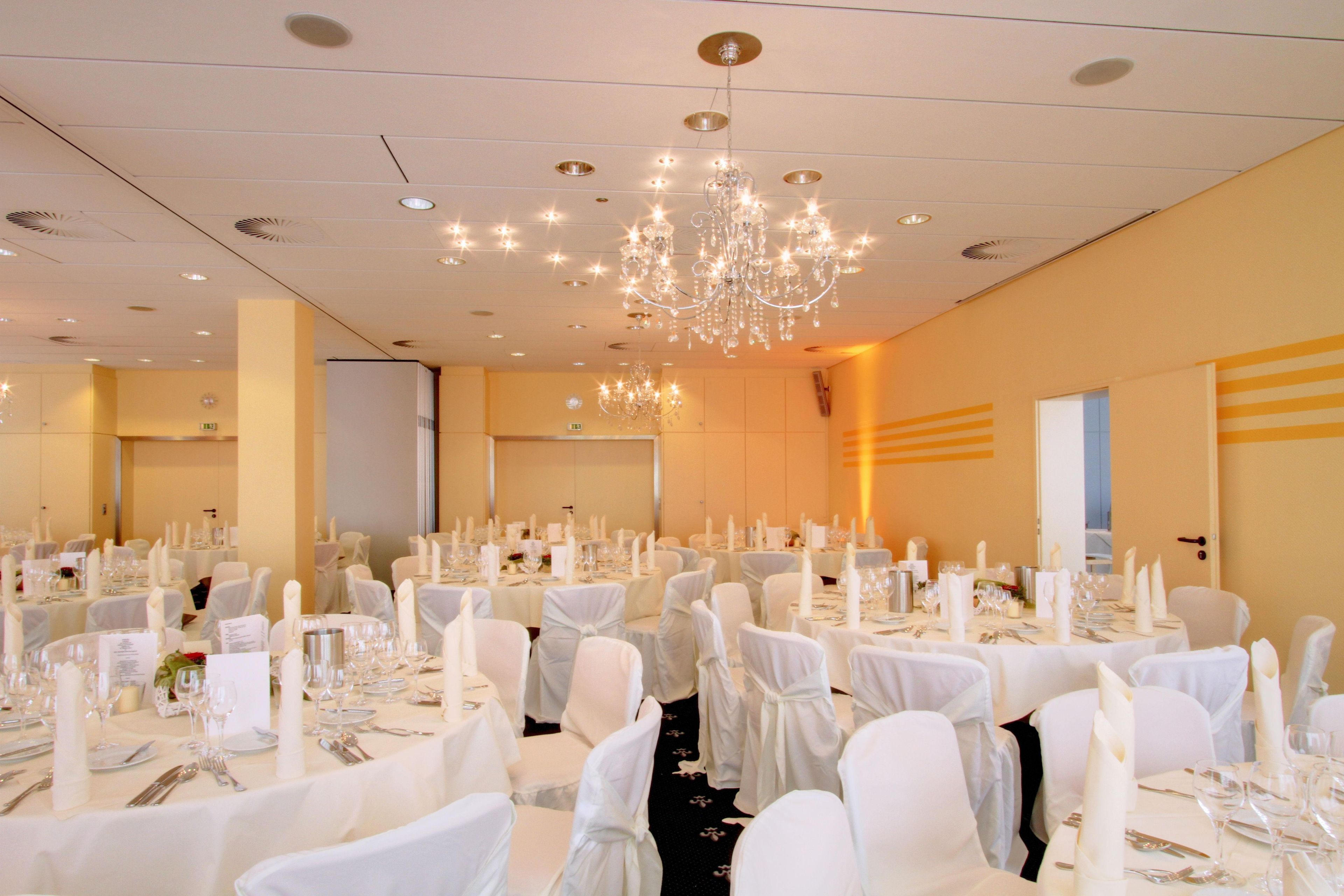 A banquet hall with round tables set for dining, white chairs, and a chandelier.