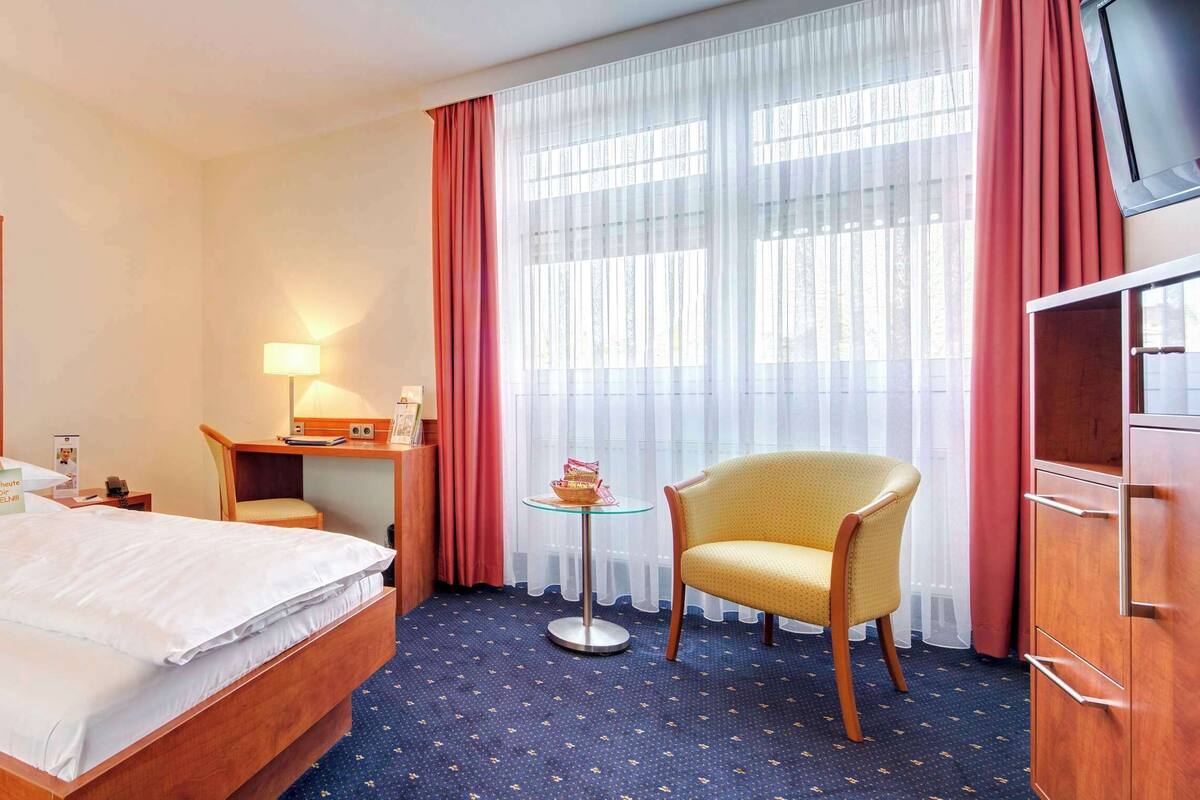 A hotel room with a bed, a desk, a chair, a TV, and a wardrobe.