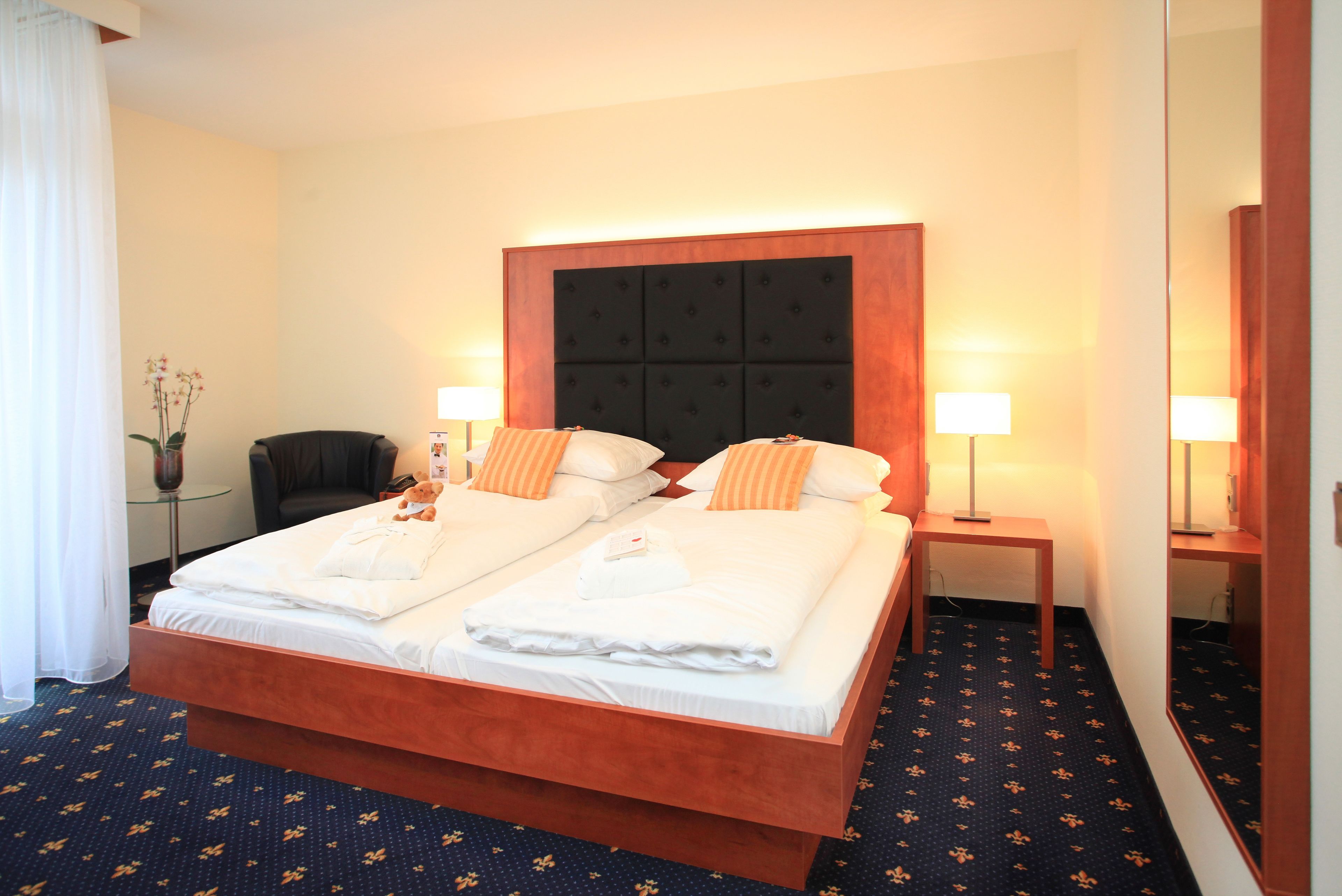 A hotel room with a double bed, two bedside tables with lamps, a chair, and a mirror.