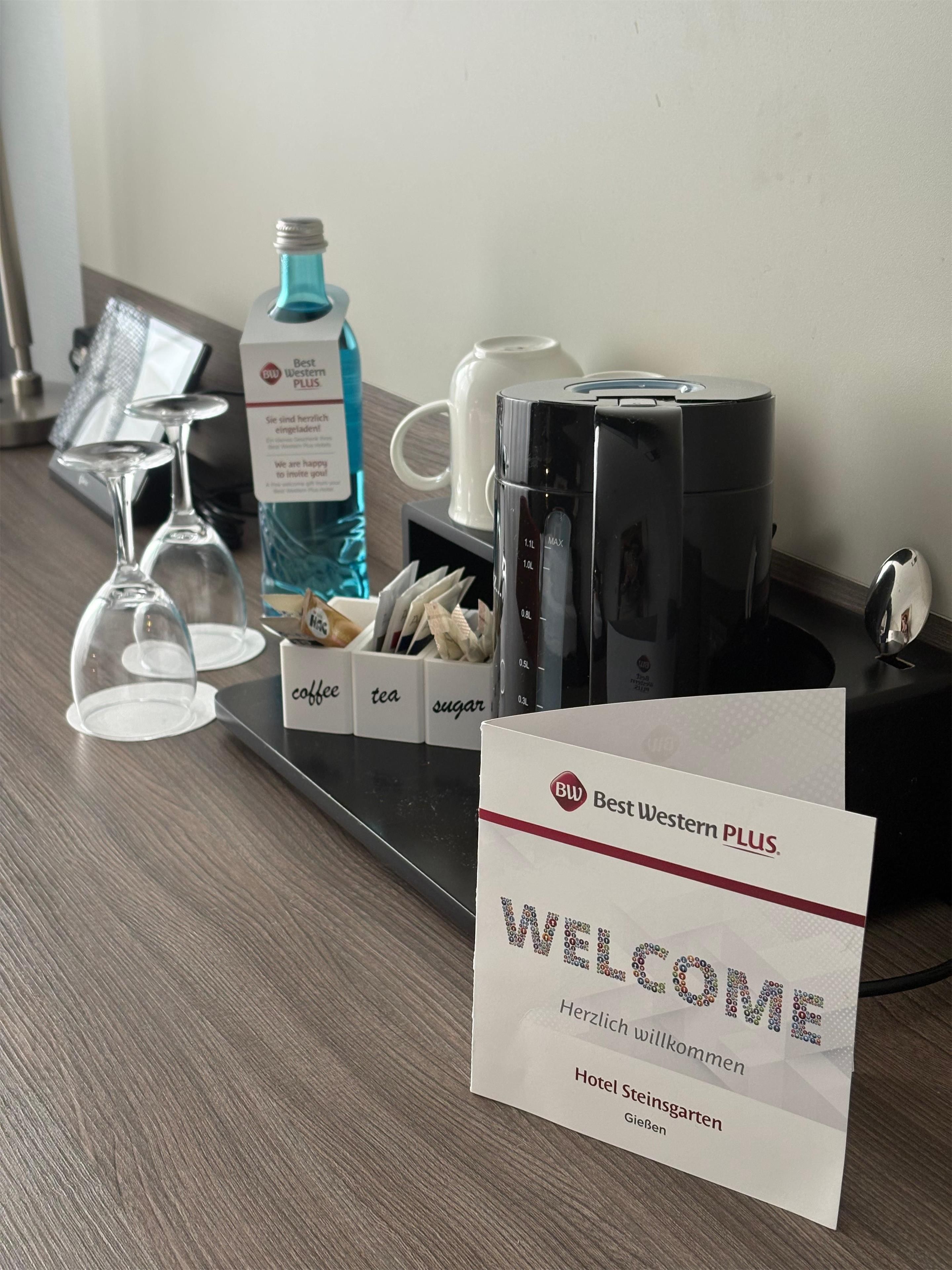 A hotel reception area with a coffee station, tea and sugar dispensers, a coffee machine, and a welcome sign.