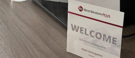 Et hotellets reception med kaffestation, te- og sukkerdispensere, kaffemaskine og en velkomstskilt.