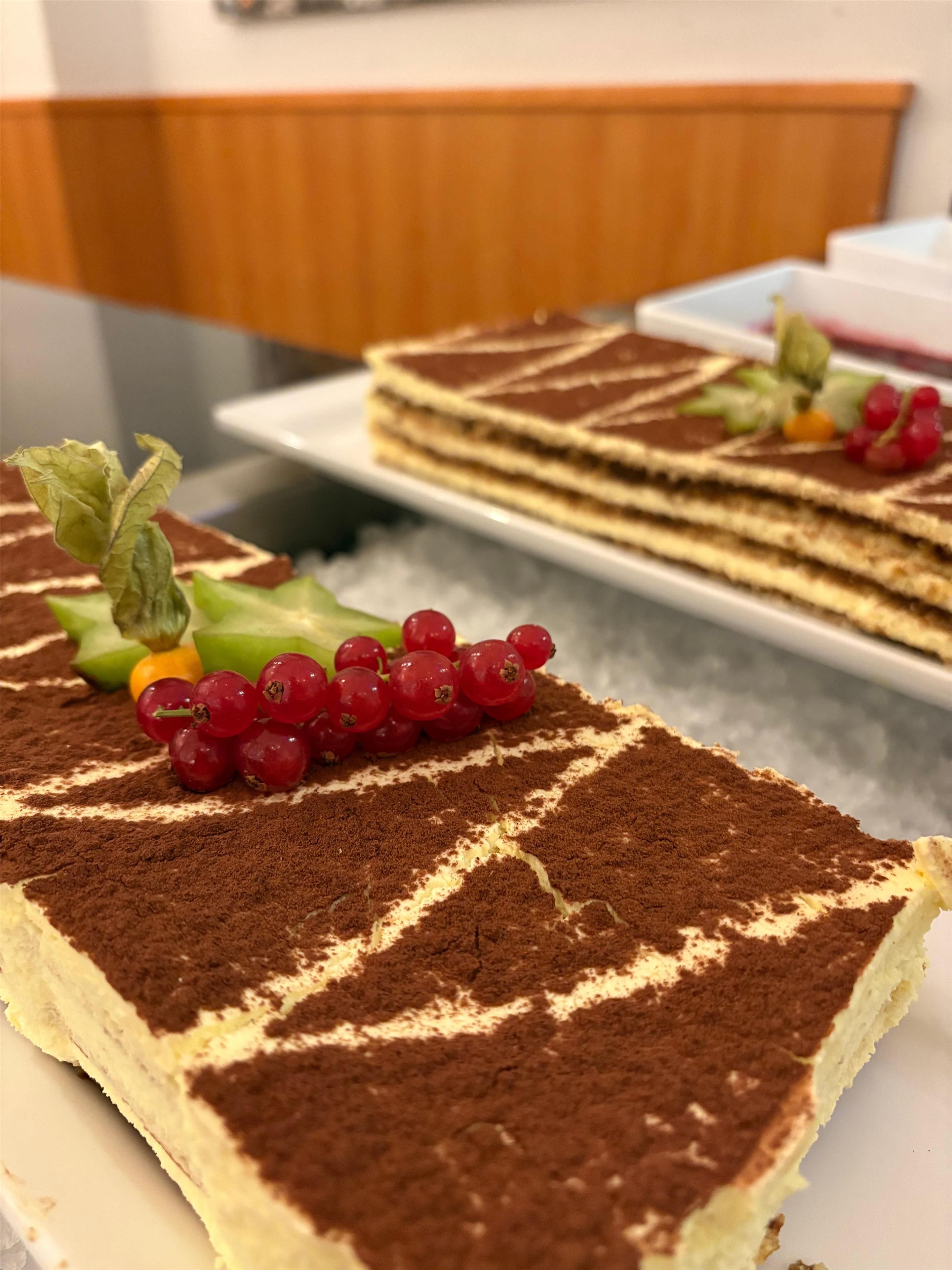 A slice of tiramisu on a plate with a decorative arrangement of red currants and a sprig of mint.