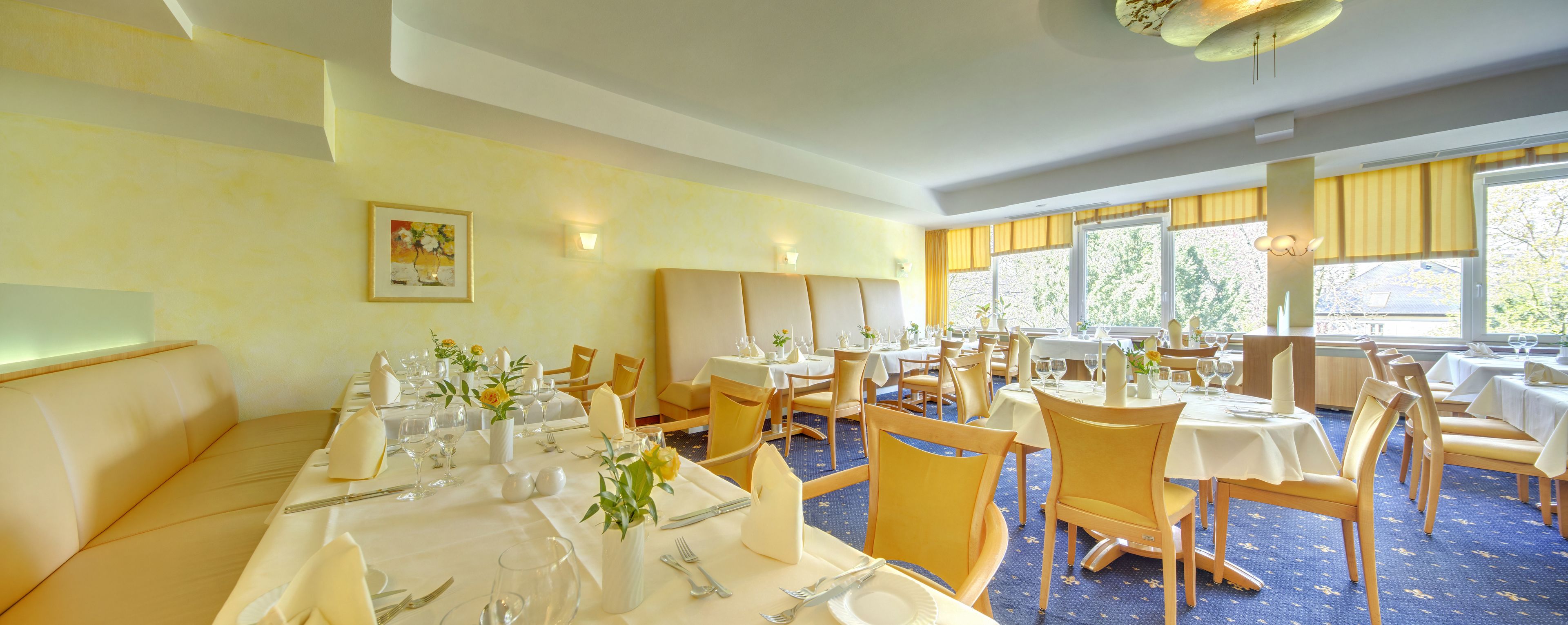 Un restaurant amb taules preparades per sopar, amb cadires grogues i tovallons blancs.