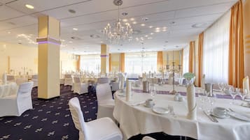 A banquet hall with round tables, white tablecloths, and chandeliers.