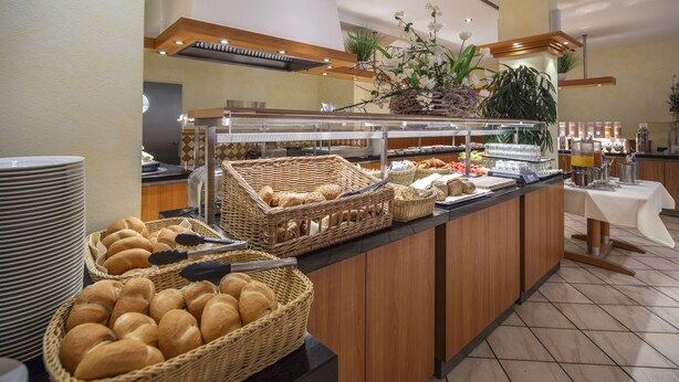 A buffet area with wicker baskets of bread, a coffee station, and a white table with a coffee machine. - Best Western Plus Hotel Steinsgarten (Giessen)