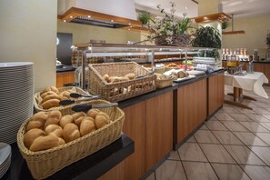Un área de bufé con cestas de mimbre llenas de pan, una estación de café y una mesa blanca con una máquina de café.