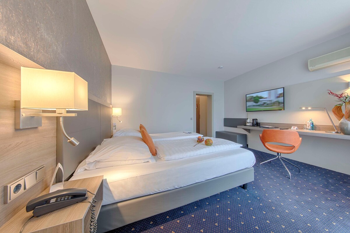 A hotel room with a bed, bedside table, lamp, chair, desk, and a TV.