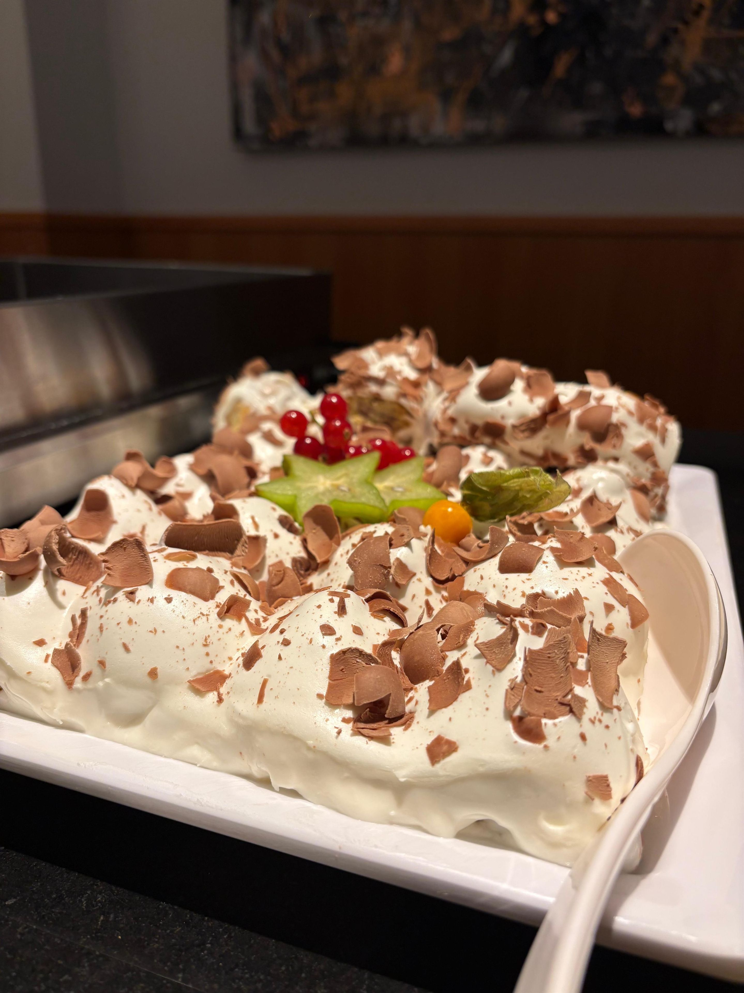 A dessert on a white plate with chocolate shavings and red berries.