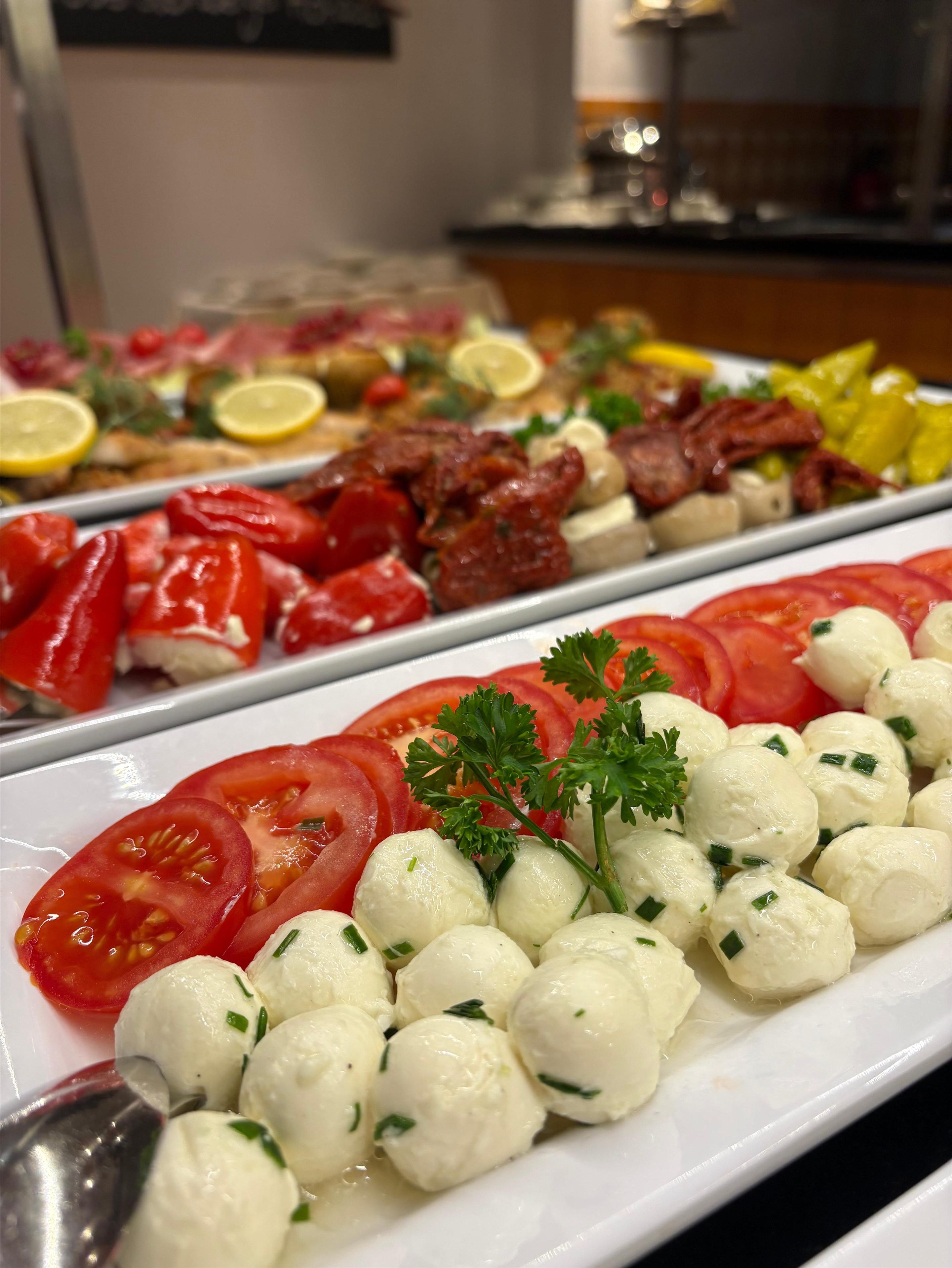 A buffet with various dishes including sliced tomatoes, meat, and a section with white spherical items garnished with herbs.
