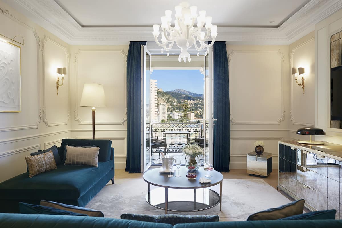 A luxurious living room with a sofa, a coffee table, and a view of a balcony with a cityscape.