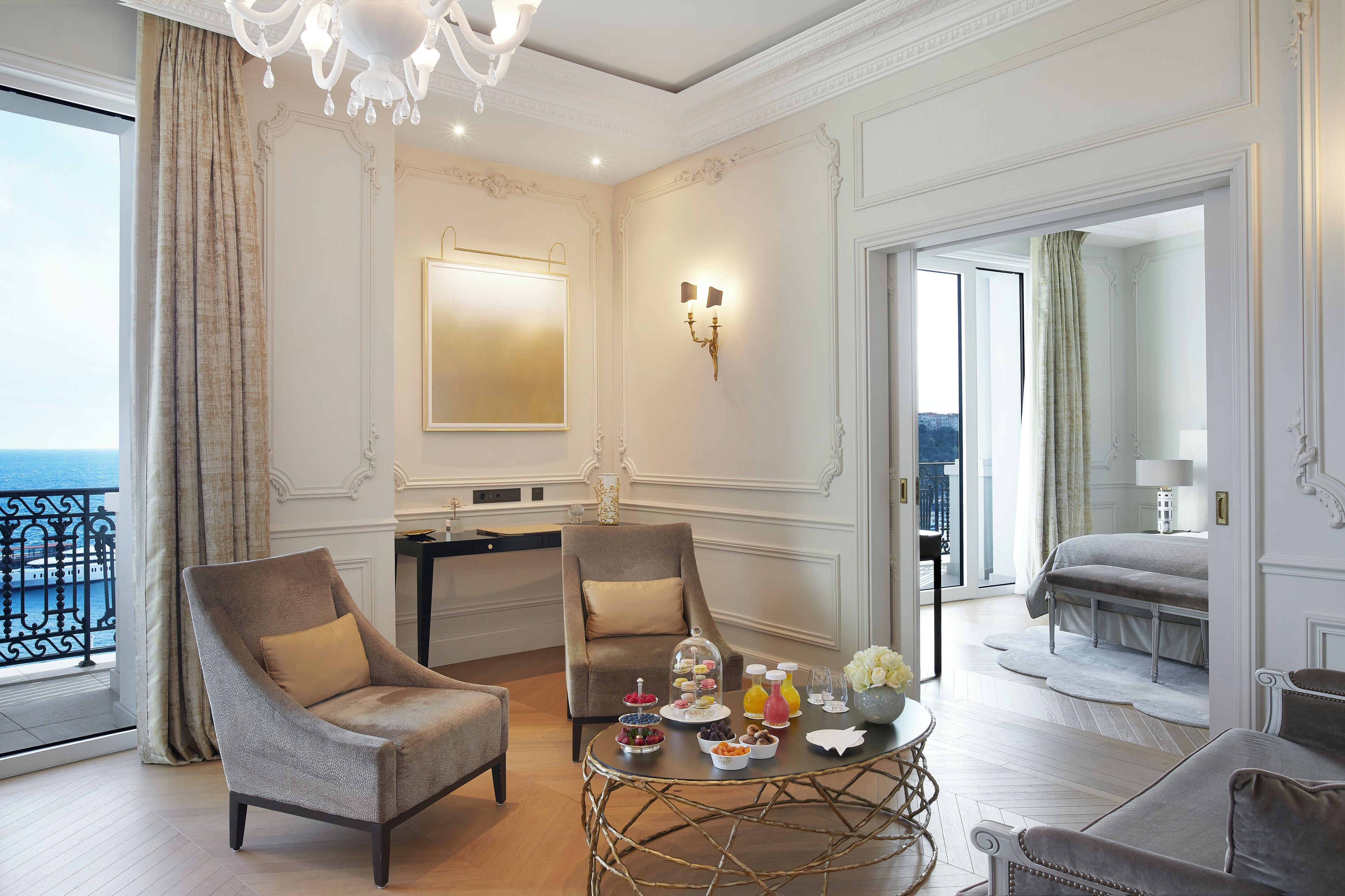 Una lujosa habitación de hotel con balcón, dos sillones, una mesa redonda con aperitivos y una cama con vistas.