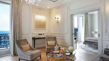Una lujosa habitación de hotel con balcón, dos sillones, una mesa redonda con aperitivos y una cama con vistas.