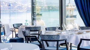 Een restaurant met gedekte tafels, met uitzicht op een waterpartij en een gebouw in de verte.