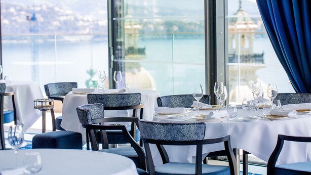 A restaurant with tables set for dining, overlooking a body of water and a distant building.