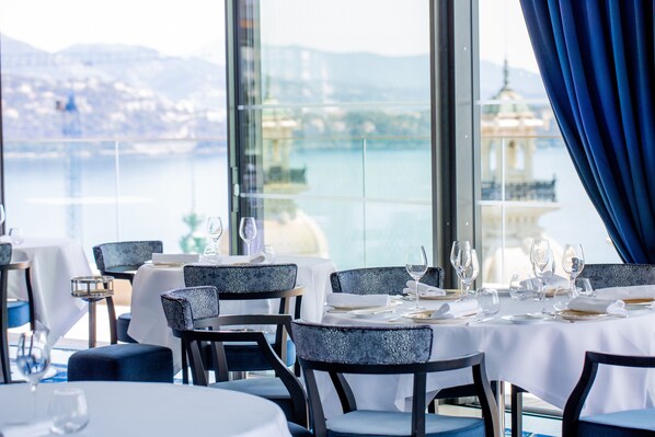 A restaurant with tables set for dining, overlooking a body of water and a distant building. - Hôtel de Paris Monte-Carlo (Monaco)