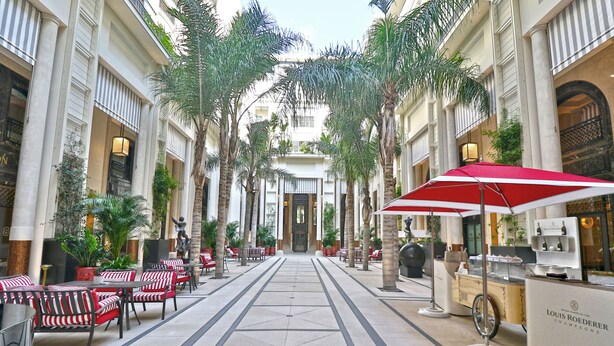 Een hotel lobby met een centrale doorgang, rode en witte streepstoelen, palmbomen en een Louis Roederer champagnebar.