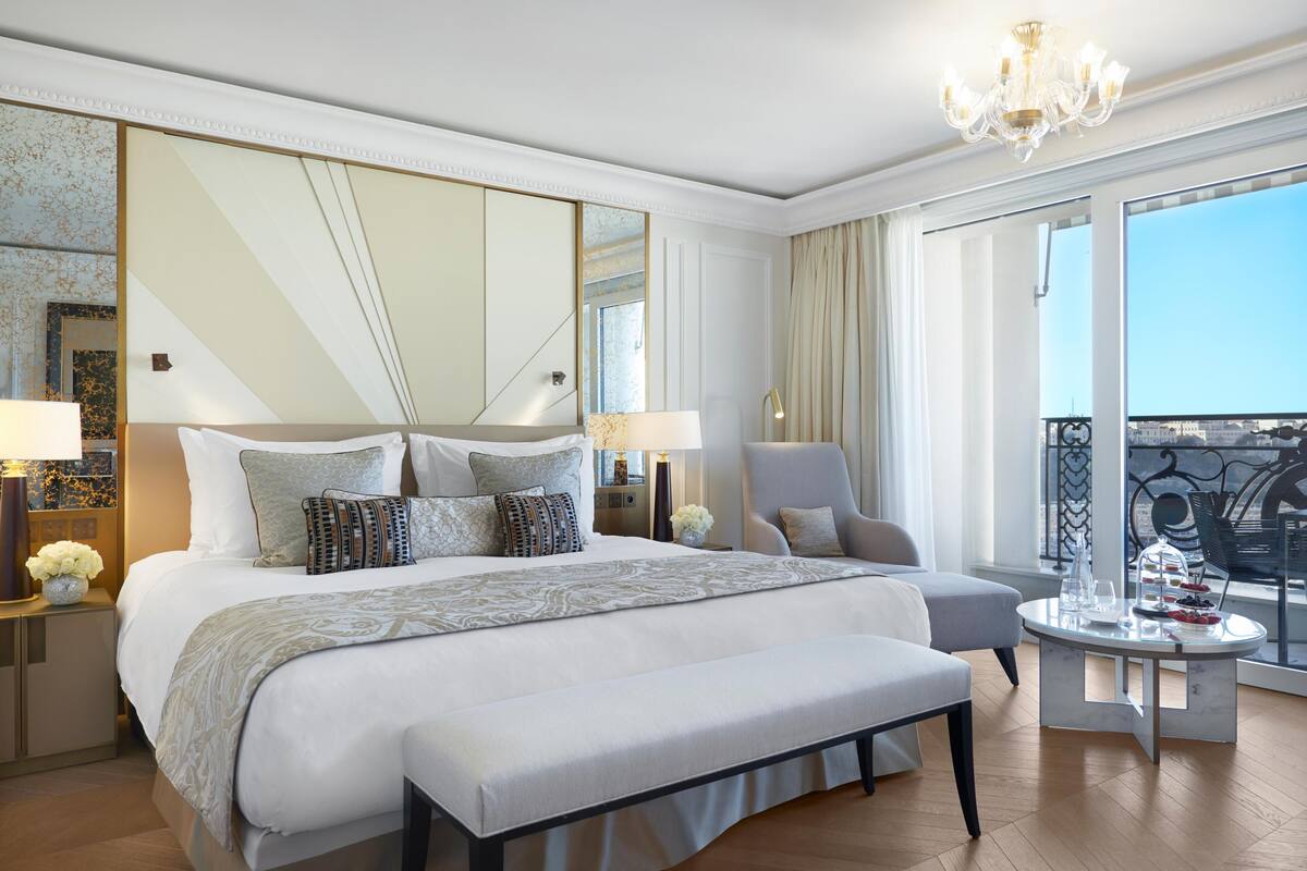 A spacious bedroom with a large bed, a sitting area, and a balcony with a city view.