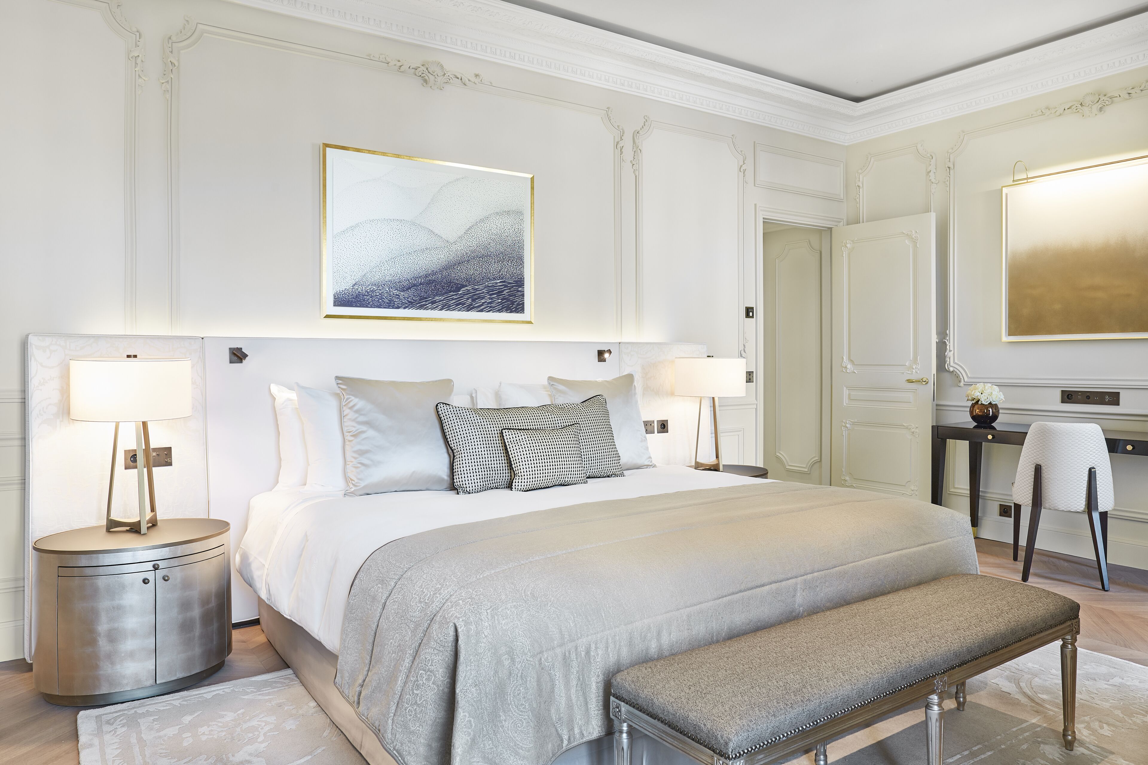 A spacious bedroom with a large bed, two bedside tables with lamps, a bench, and a desk with a chair.