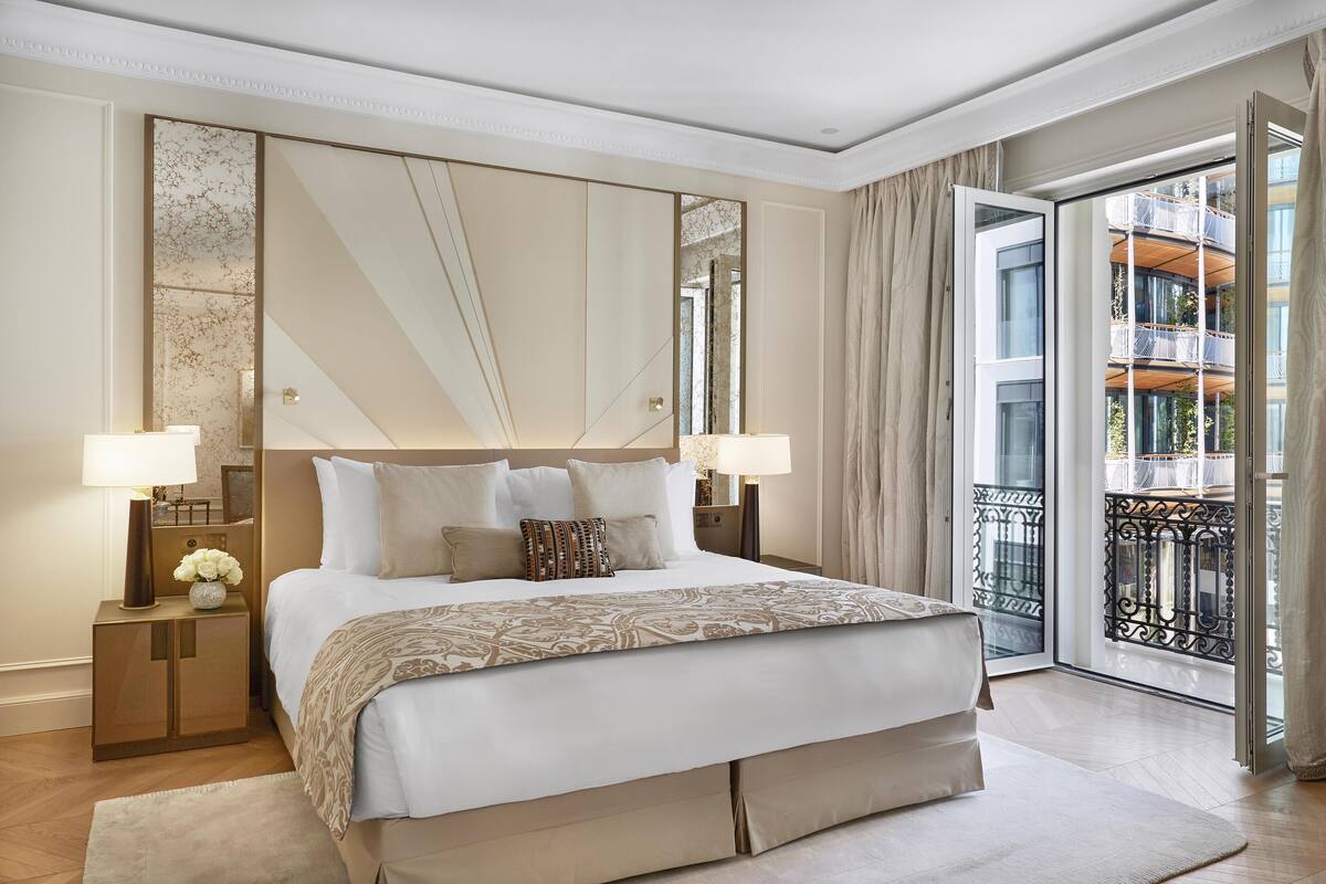 A spacious bedroom with a large bed, two bedside tables, a mirror, and a view of a balcony.