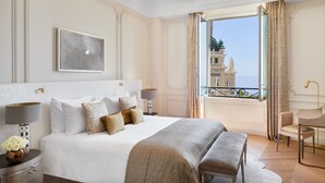 A hotel room with a large bed, a bedside table with a lamp, a chair, and a view of a building through a window.