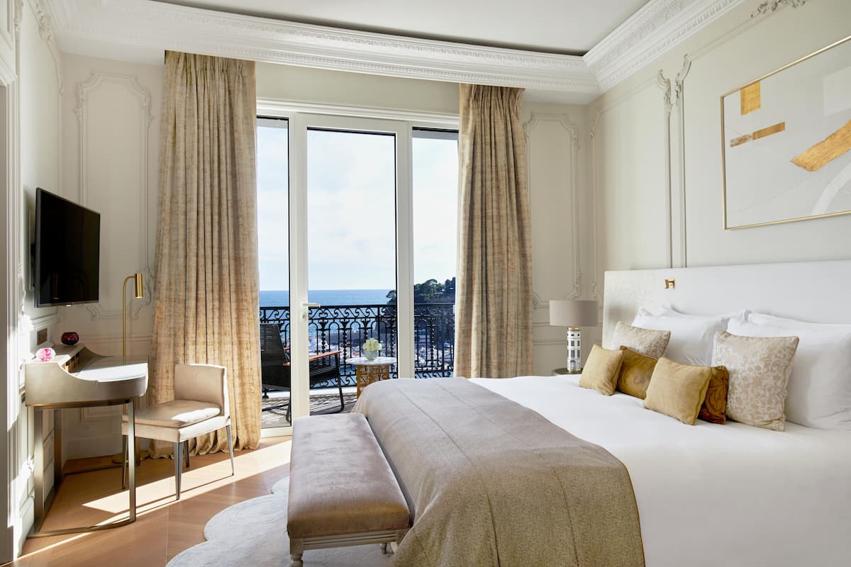 A hotel room with a large bed, a desk, a chair, a bench, and a TV.