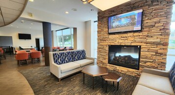 A modern lounge area with a stone wall, a flat-screen TV, a fireplace, and seating arrangements.