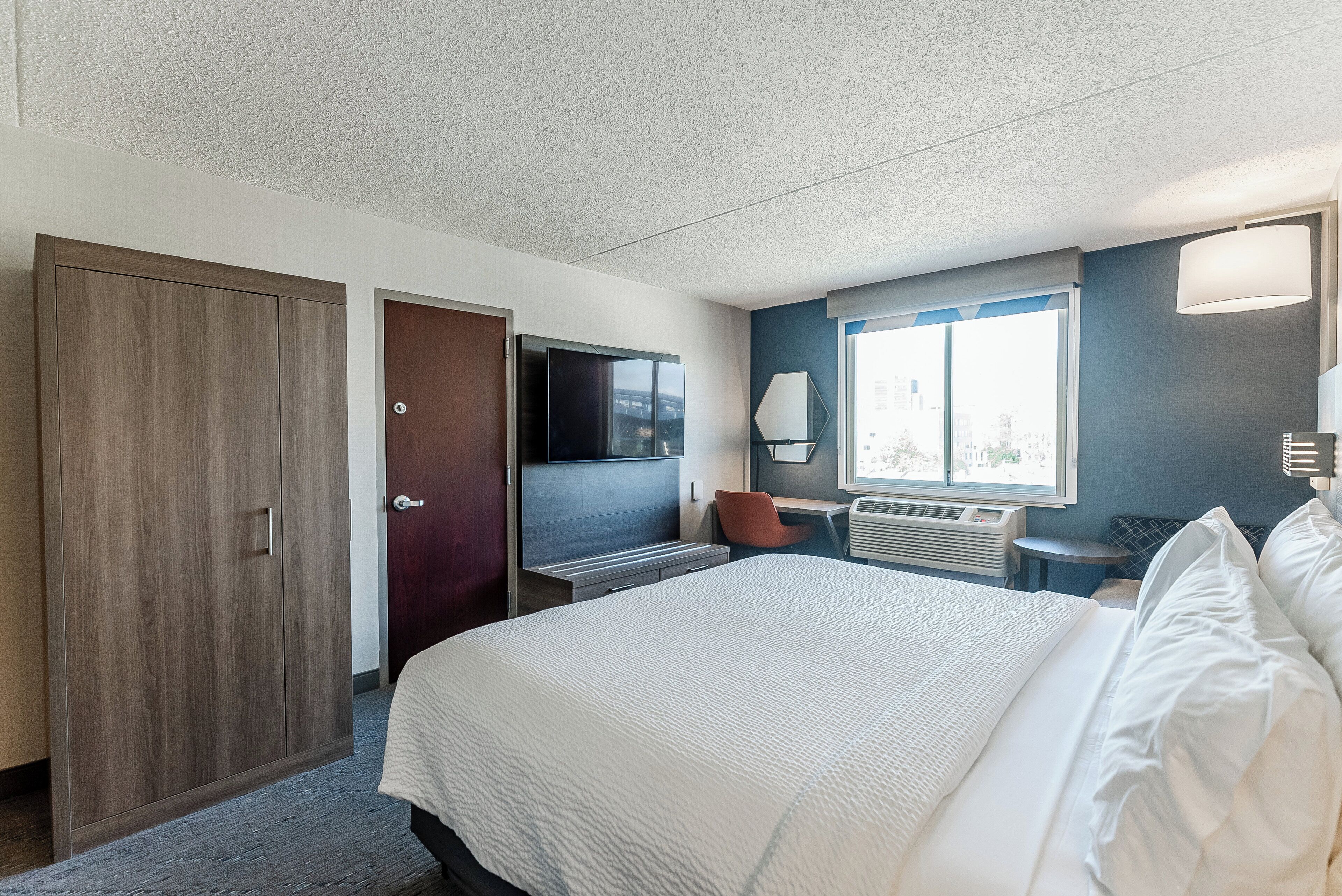 A hotel room with a large bed, a desk with a chair, a wardrobe, and a television.