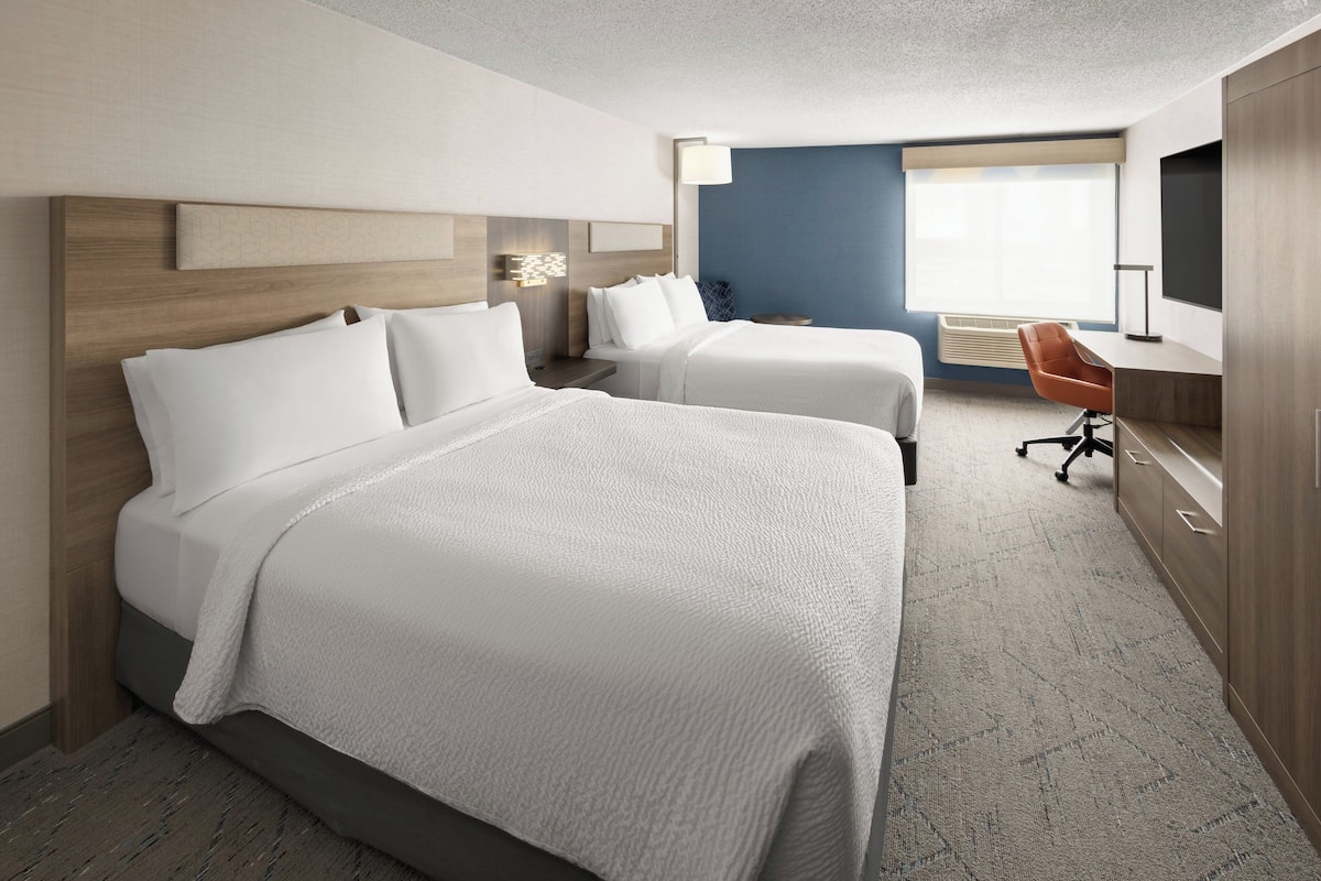A hotel room with two beds, a desk, a chair, and a TV.