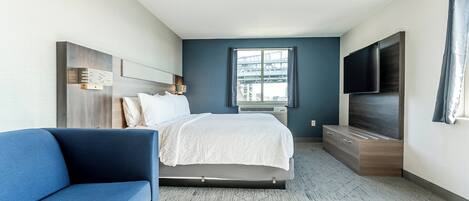 A modern hotel room with a bed, a blue sofa, a flat-screen TV, and a large window.