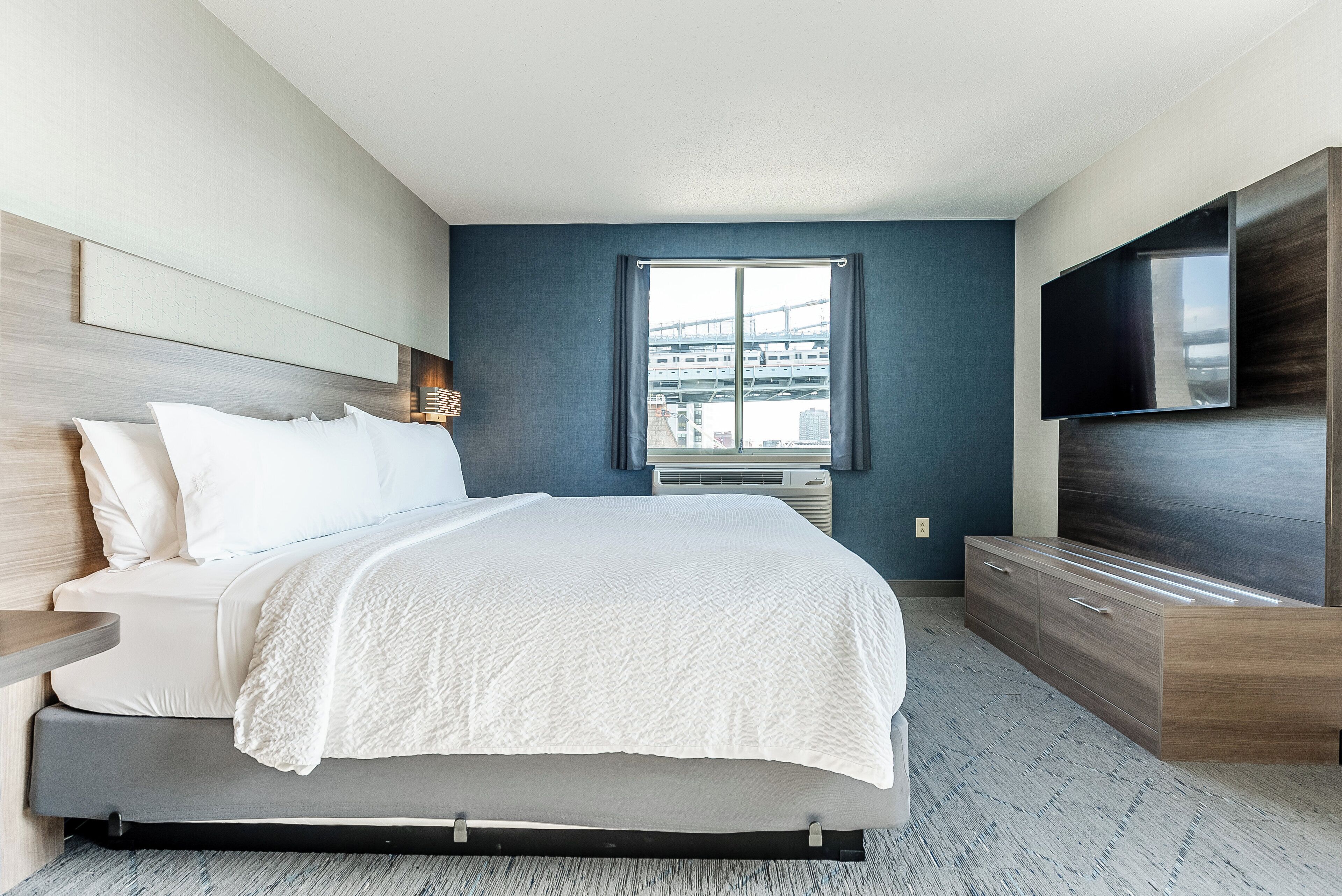 A modern bedroom with a bed, a TV, and a window with a city view.