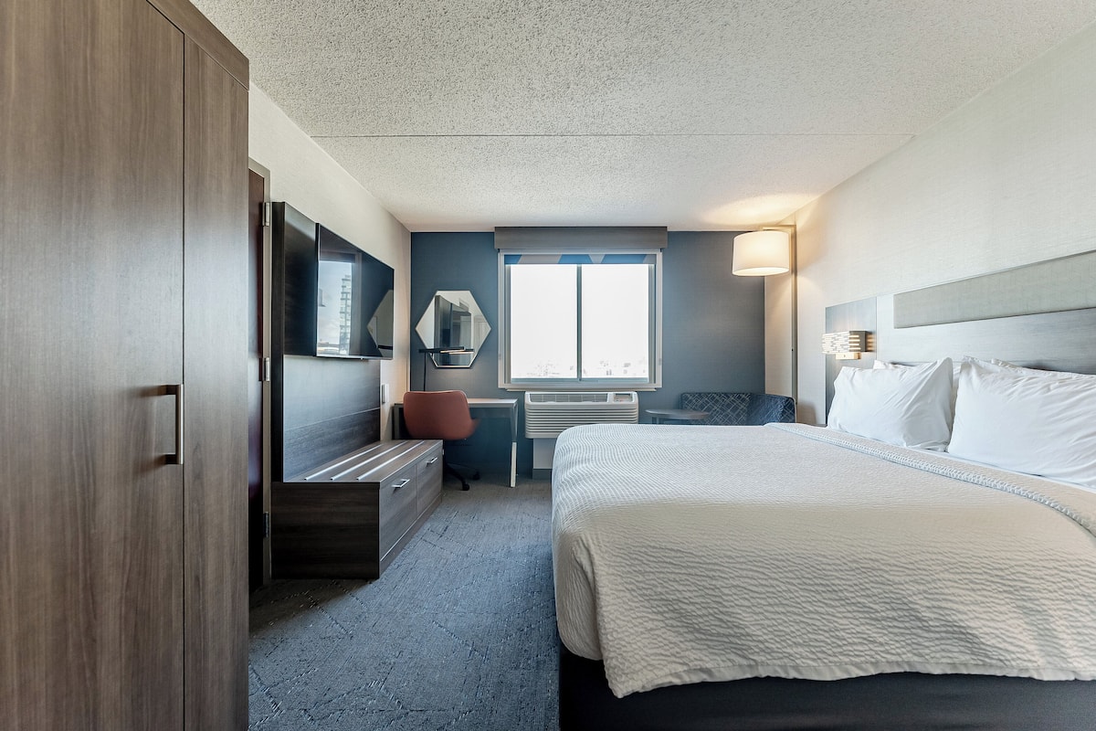 Relax in a spacious room with a large bed, desk, and wardrobe, offering a clean and minimalist design for a comfortable stay.