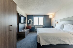 A modern hotel room with a large bed, a desk with a chair, a wardrobe, and a large window.
