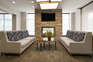 A lobby with two sofas, a small table, a potted plant, and a TV mounted on a stone wall.