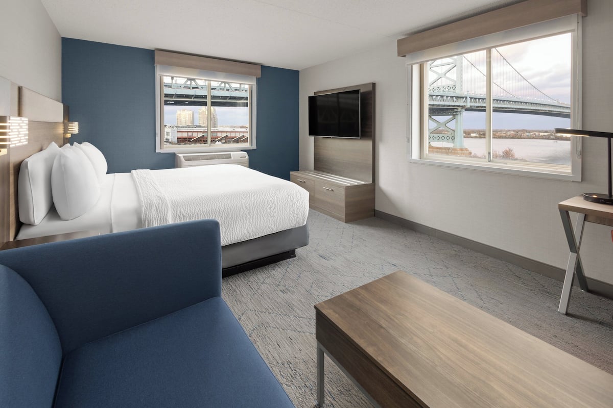 A hotel room with a bed, a TV, a desk, and a view of a bridge.