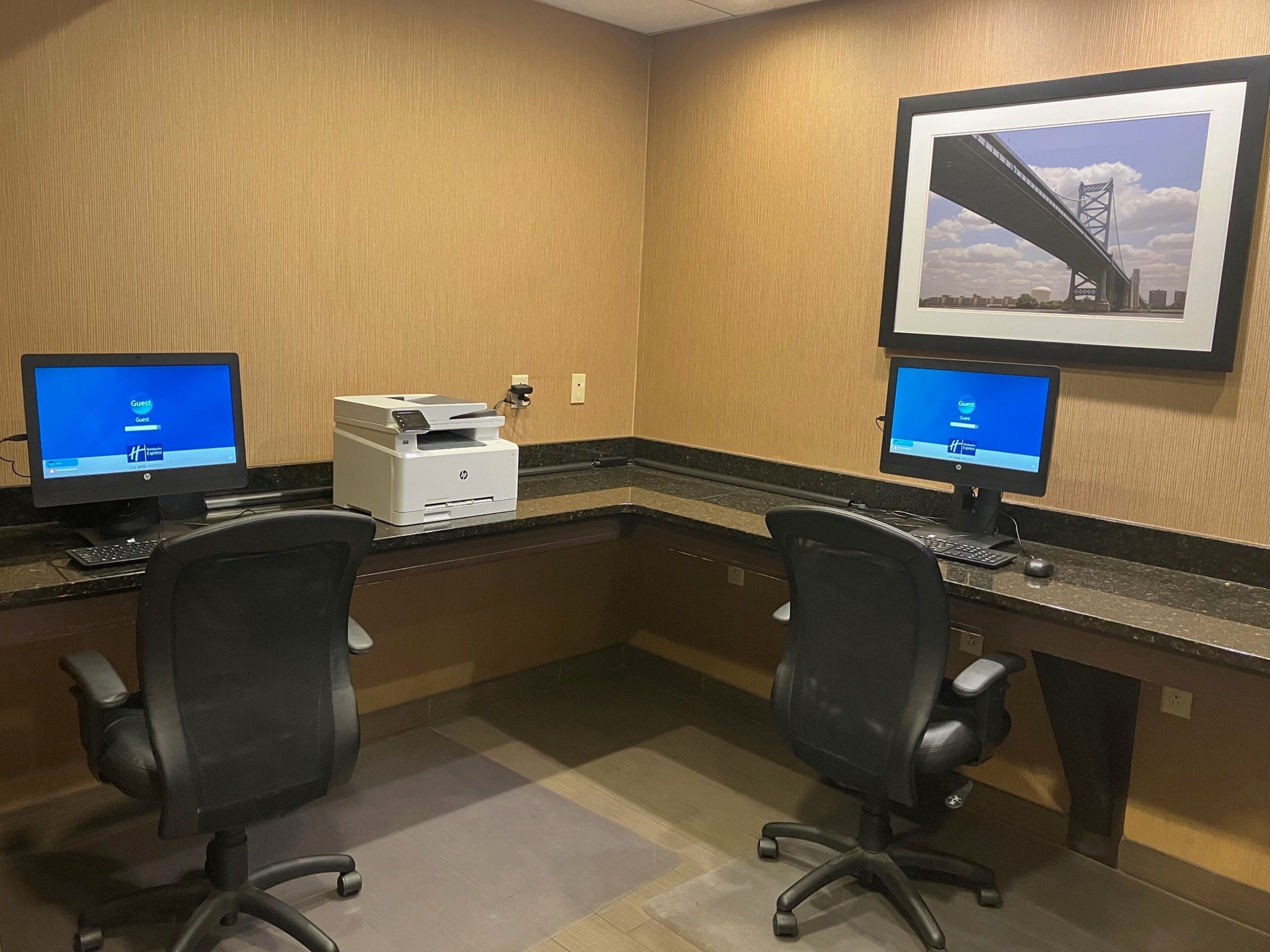 A hotel office with two HP printers, two computer monitors, and two office chairs.