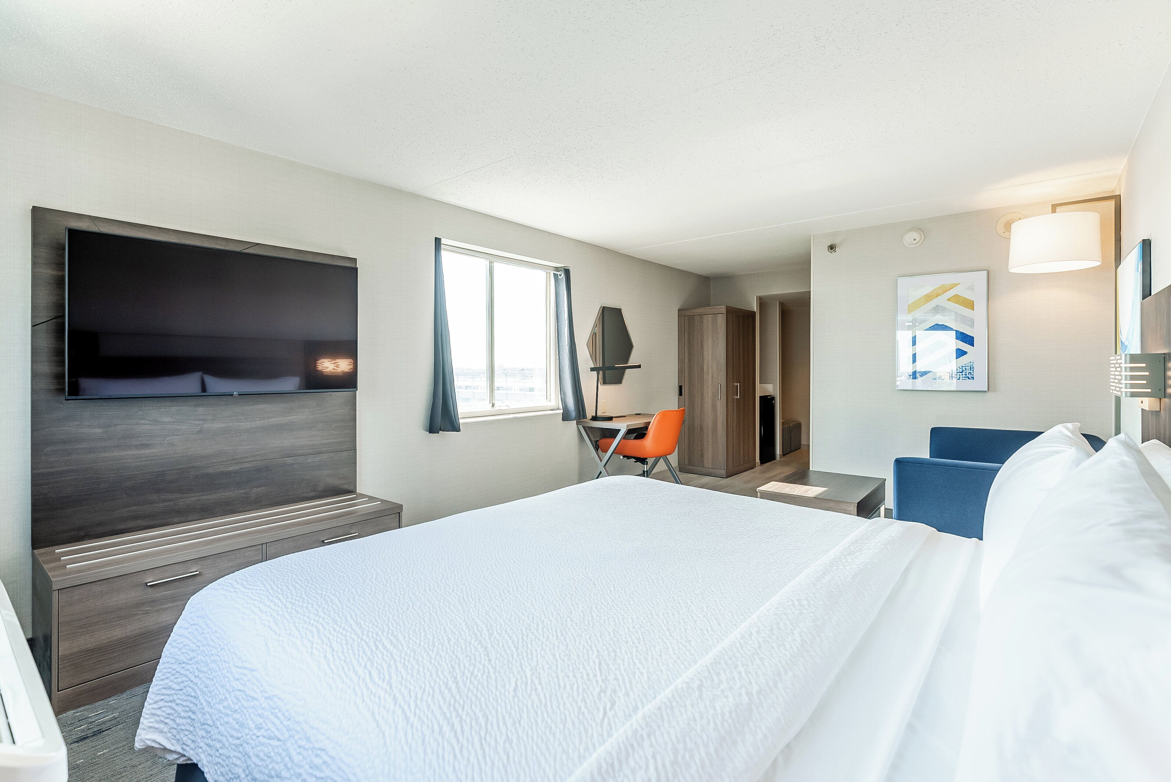A hotel room with a large bed, a desk, a chair, and a TV mounted on the wall.