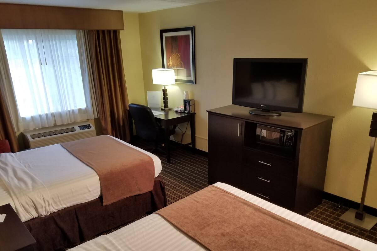 A hotel room with two beds, a desk, a television, and a lamp.
