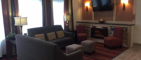 Habitación de hotel con sofá, dos sillones, televisor de pantalla plana y chimenea.