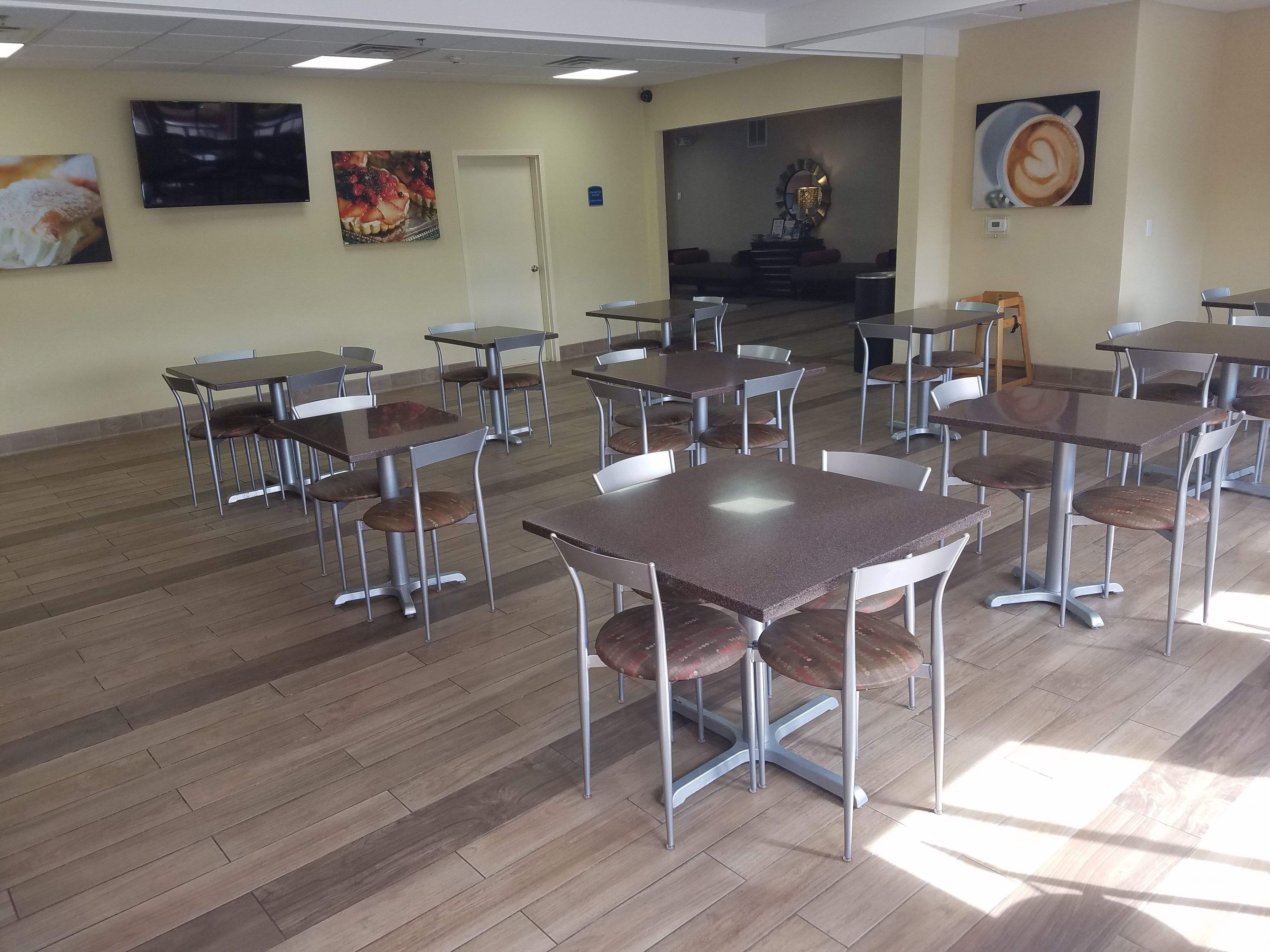 A spacious dining area with multiple tables and chairs, a wooden floor, and wall art.
