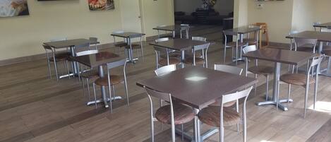 A spacious dining area with multiple tables and chairs, a wooden floor, and wall art.