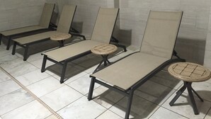 A row of four lounge chairs with cushioned seats and backs, arranged in a row against a tiled wall.