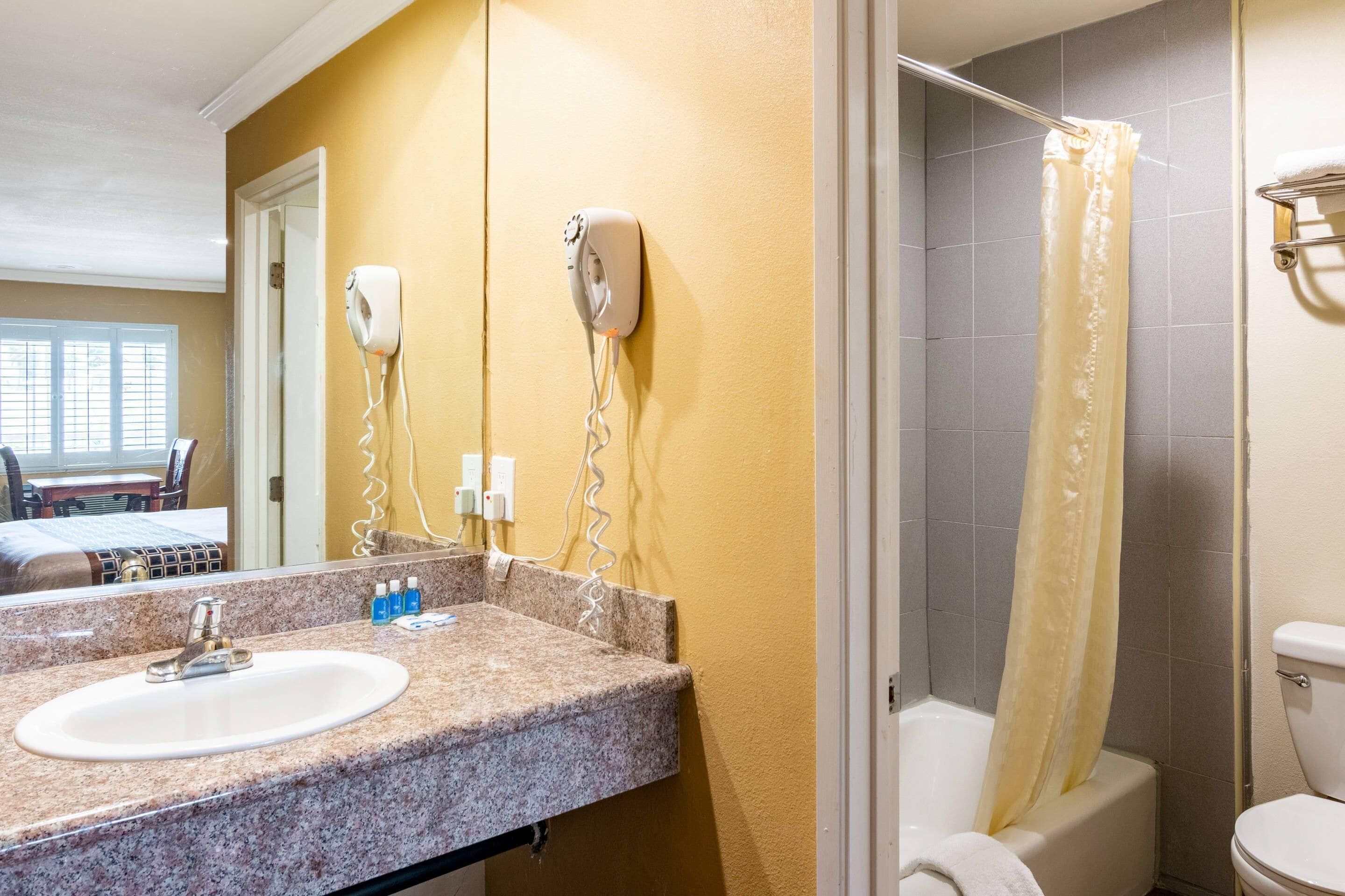 A bathroom with a sink, two hair dryers mounted on the wall, a shower curtain, and a toilet.