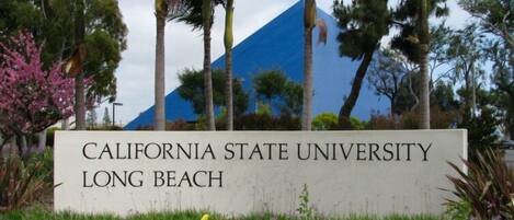 A sign for California State University Long Beach with a blue building in the background.