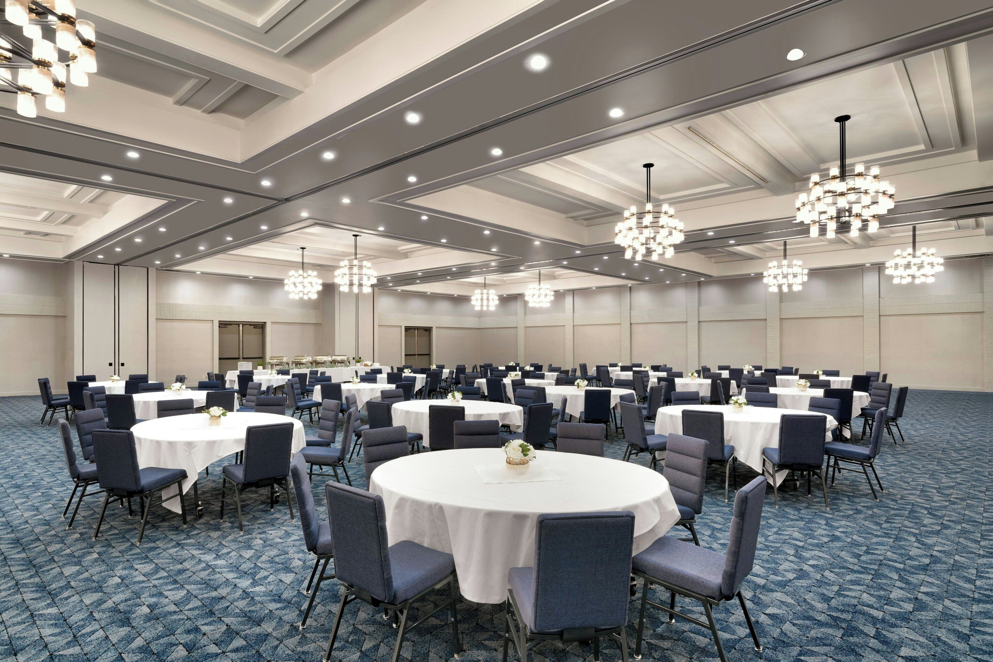 A large conference room with round tables and chairs, ceiling lights, and a carpeted floor.