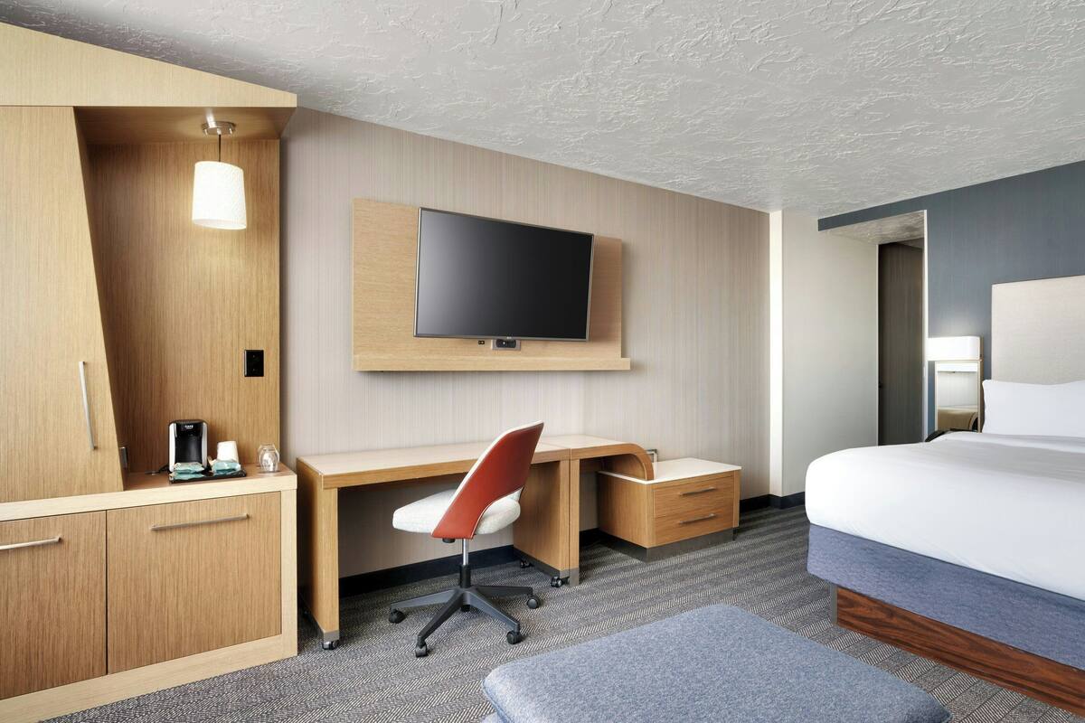 A hotel room with a bed, a desk with a chair, a television, and a wardrobe.