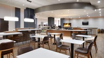 A modern restaurant with a curved ceiling, multiple seating areas, a bar, and a television screen.