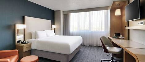 A hotel room with a large bed, a desk with a chair, a television, and a window with curtains.